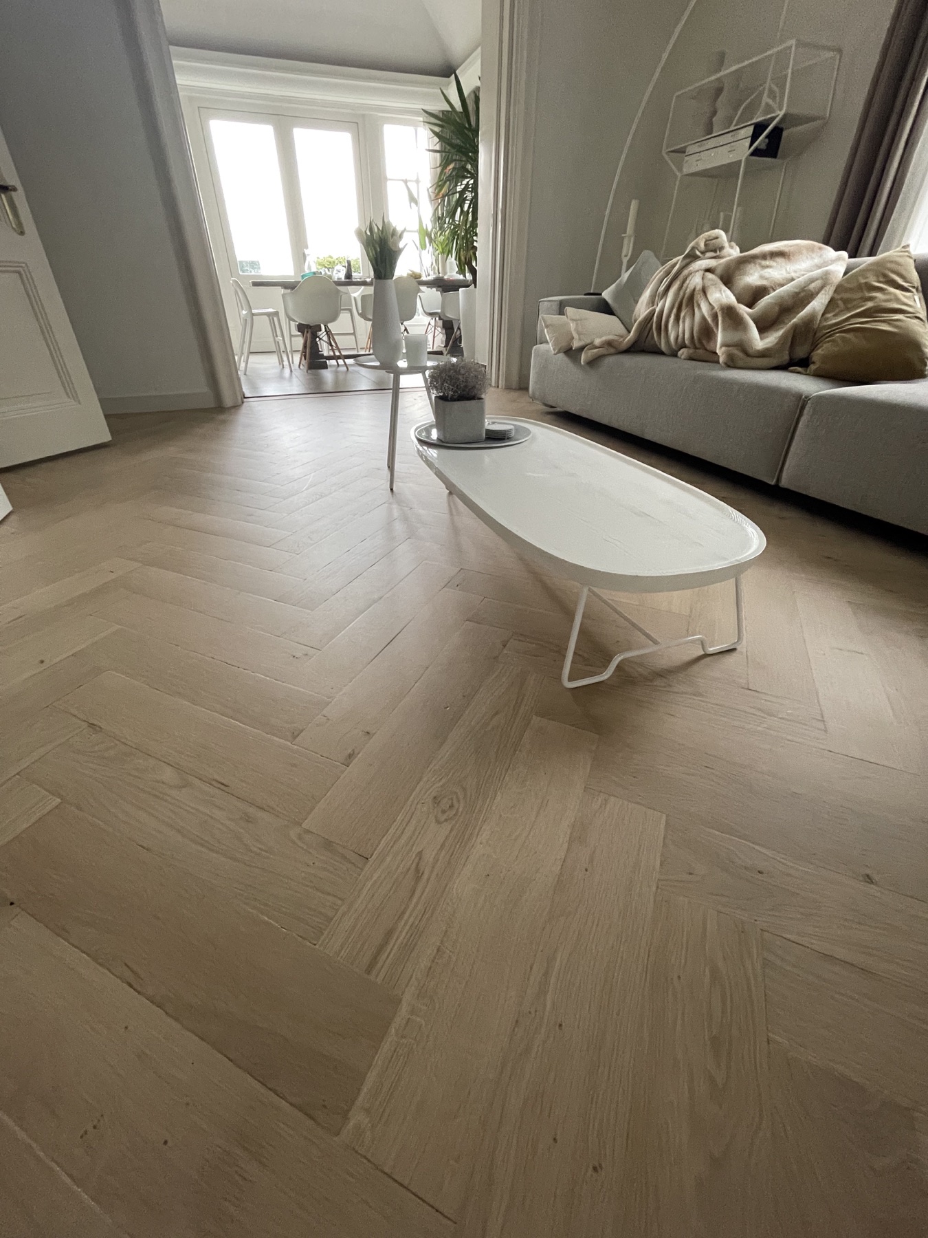 Lichte houten visgraatvloer in een woonkamer met grijze bank en witte salontafel